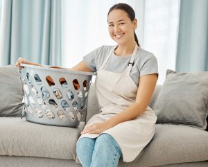 Cleaning, laundry and happy asian woman with on the sofa with a basket about to do washing of fold
